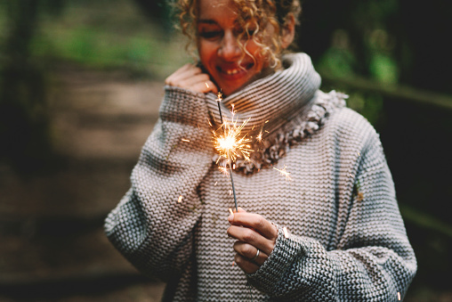 Happy woman celebrating outdoor with sparkler fire and smile. Concept of people and celebration. Birthday and new year eve. One female alone enjoy life in autumn. Green background nature