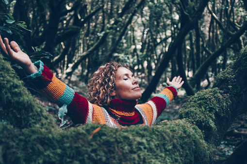 Overjoyed young woman outstretching and opening arms for joyful emotions. Happy female people loving nature and trees at the park. Green color. Adventure and alternative tourism. Environment concept