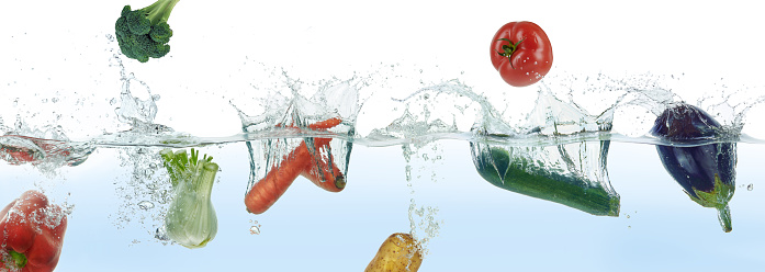 Mix of different vegetables splashing in water. Side panoramic view on white background.