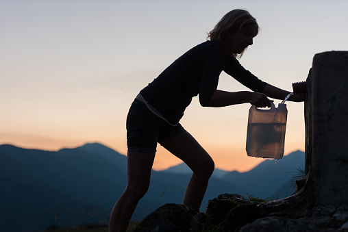 Woman at the Sunset Filling Mountain Spring Water in a Plastic Water Jug