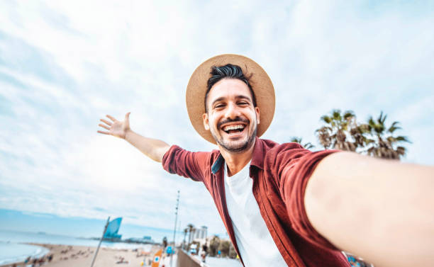 homem bonito tirando selfie na cidade de barcelona, espanha - feliz turista se divertindo andando fora nas férias de verão - viagens, férias e marcos europeus conceito - mid adult men portrait hat human face - fotografias e filmes do acervo