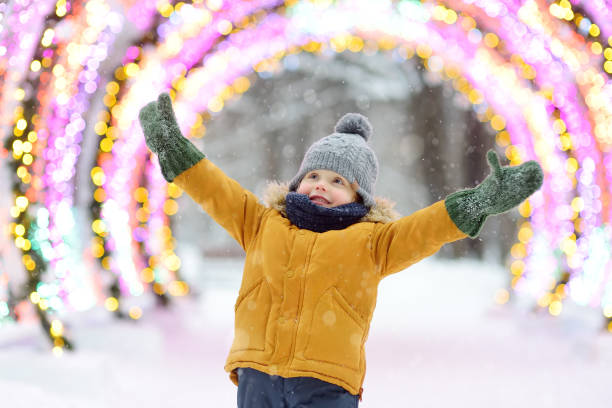 il ragazzino sta ammirando una grande decorazione di strada incandescente alla fiera di natale. tradizionale mercato natalizio della città all'aria aperta. decorazione festiva urbana moderna. - snow festival foto e immagini stock