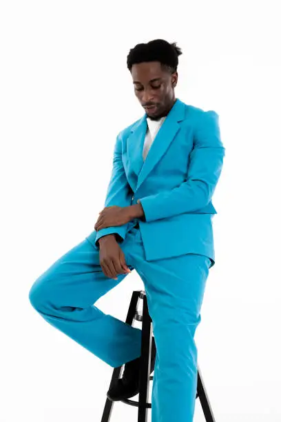 Dark-skinned man model looking-down posing sitting on chair wearing funny hairstyle and casual lifestyle blue suit on white background in studio isolated.