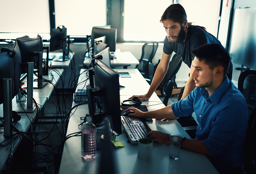 Closeup side view of two young men coding on multiple computers at a software developing office.