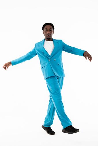 Good-looking african american man looking at camea posing for fashion magazine wearing smart casual blue suit and white t-shirt spreading hands to the side crossing legs. Dark skinned model good mood.