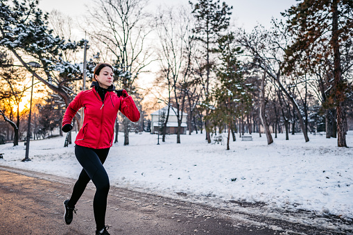 Beautiful young woman jogging in a snowy park during winter.