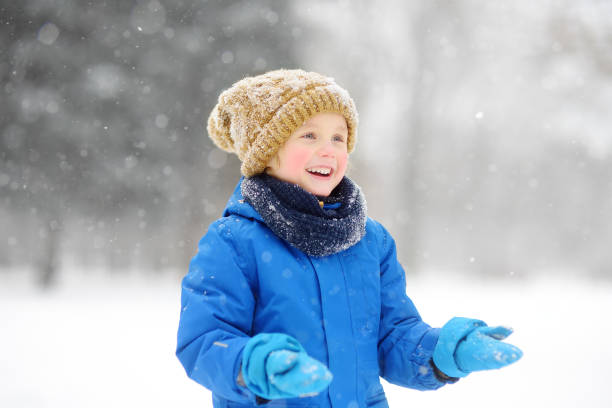 istock Little boy having fun playing with fresh snow during snowfall. Baby catching snowflakes on gloves. Kid dressed in warm clothes, hat, hand gloves and scarf. Active winter outdoors leisure for child 1431317454