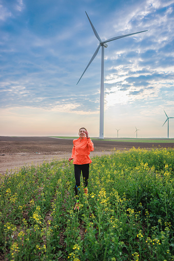 Running through the plants in the agricultural field with wind turbines under the cloudy blue sky, cross-country running