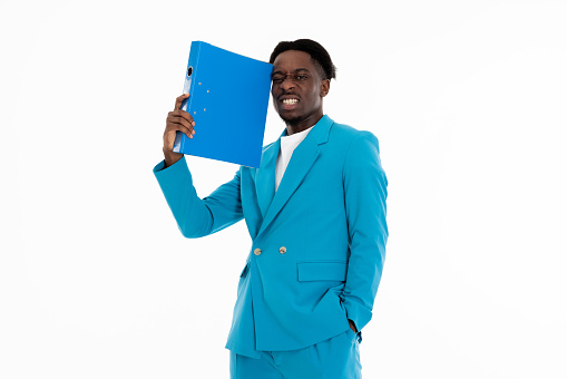 Portrait of african american man holding folder in arm showing angry emotions at camera posing in blue suit and white t-shirt standing on white background in studio isolated.
