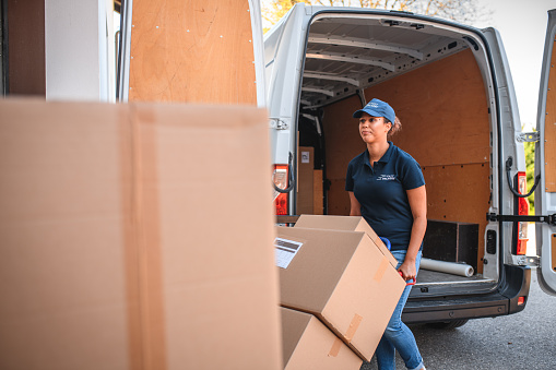 Female delivery worker standing behind a full stack of boxes, in front of white van.