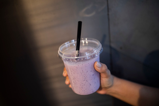 Close-up of female hand holding disposable cup with strawberry milkshake