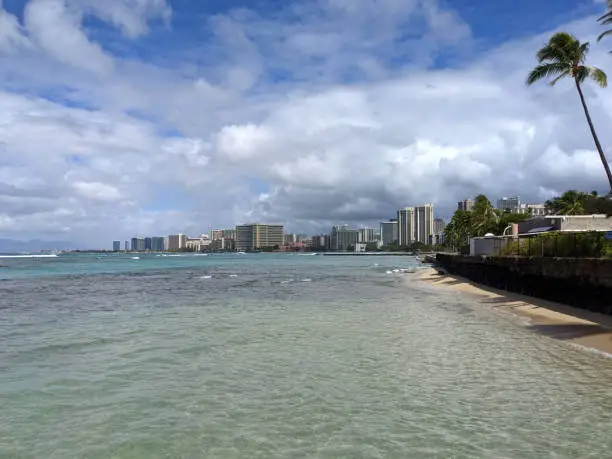 Sans Souci Beach, walkway, and ocean water with Waikiki hotels in the distance.