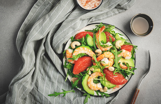 Healthy fresh salad with shrimps, avocado, grapefruit, arugula and cashews. Gray stone kitchen  table background, top view, copy space