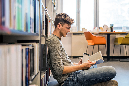 Student in library reading book from bookshelf