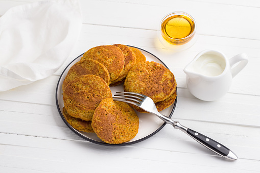 Healthy pumpkin pancakes with oatmeal served with honey and cream on a white background. Delicious vegetarian food
