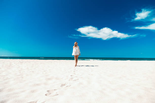 woman on sea beach single happy young woman in swimsuit and white blouse at sand sea beach with blue clean sky walking beach women sadness stock pictures, royalty-free photos & images