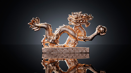 Luxurious antique golden dragon statuette on a black background in professional illumination