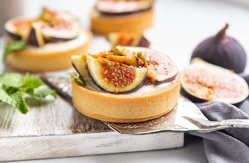 Tartlets with delicate cream cheese and fresh figs decorated with mint and pistachio, gray background. Autumn dessert. National Dessert Day, October 14.