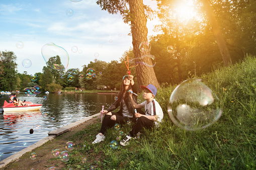Mom and teen son having fun on green lawn with soap bubbles in spring public park, together in sunny day. Family having rest and fun in good summertime. Concept motherhood, childhood. Copy text space