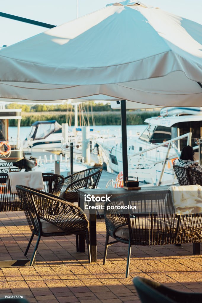 Outdoor terrace of restaurant or cafe. Blankets hang on the backs of the chairs. Background with a view of the yacht club. Outdoor terrace of a restaurant or cafe. Blankets hang on the backs of the chairs. Background with a view of the yacht club. Dining Stock Photo