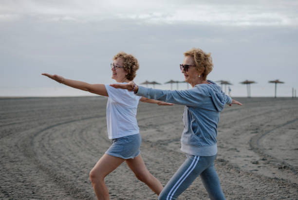 Two older women on the beach practicing yoga. Concept of mental health stock photo