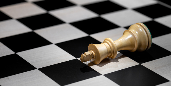 White king piece laying on chess board after losing game. Strategy, risk management and leadership concept.