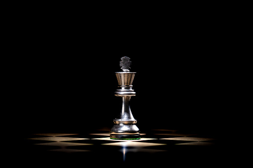 Close-up of glossy chess piece on game board lit by spotlight. Black king against black background. Strategy, risk management and leadership concept.