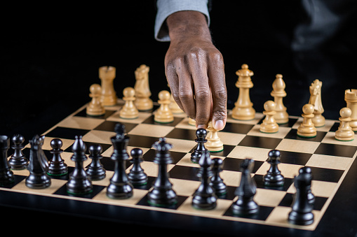 Black man playing chess. Hand moving white chess pieces on chessboard. Strategy, risk management and leadership concept.