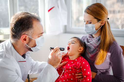 Pediatrician examining little girls throat