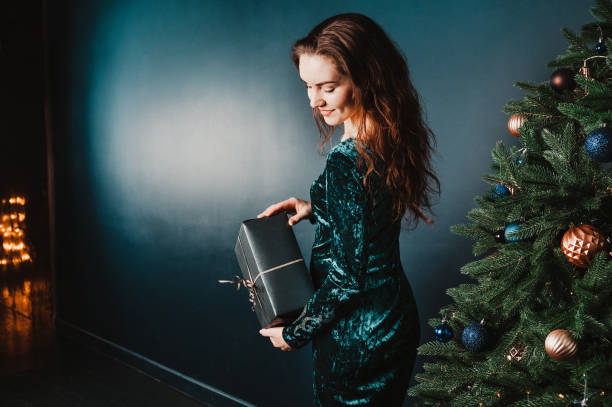 istock young woman holding gift box near Christmas tree 1431352593