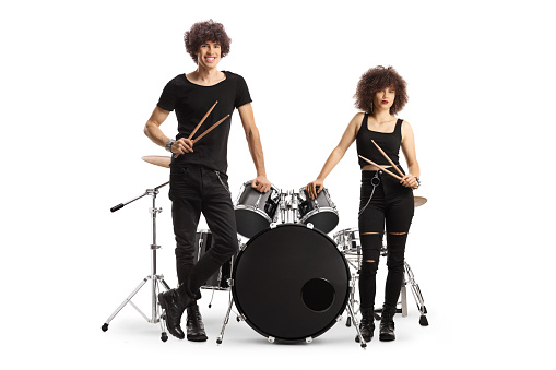 Male and female drummers standing next to a drum kit and holding drumsticks isolated on white background