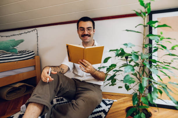 istock Fashionable hipster man with mustache reading a book while at home. 1431359650