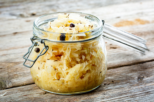 Homemade sauerkraut with cumin and juniper berries in a glass jar, closeup