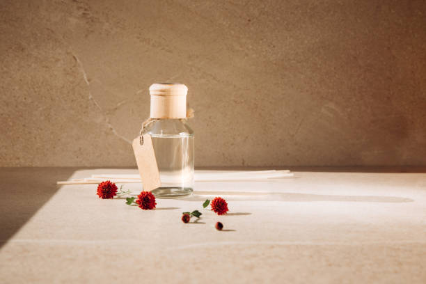 istock Aroma diffuser in a clear glass bottle with a wooden cap on a light stone background with wooden sticks behind and red chrysanthemum flowers 1431366318