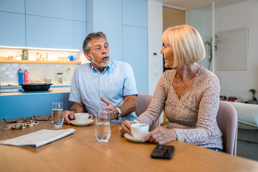 Side View Of A Senior Couple Talking In The Kitchen And Holding Coffee Cups