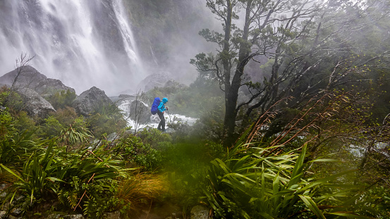 Woman backpacker hiking in front of raging Earland Falls, Routeburn Track, Fiordland National Park, New Zealand.