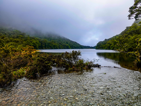 River flowing out of a misty Lake Howden. Routeburn Track, Fiordland National Park, New Zealand.