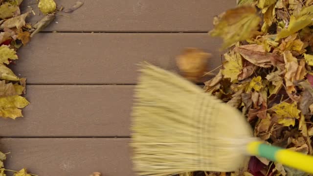A broom sweeping fallen Autumn leaves from a composite deck.