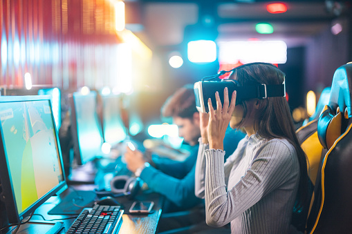 Female gamer wearing virtual reality headset for playing video games in entertainment club.