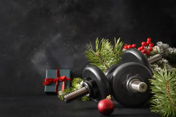 Photo of Christmas sport composition with blue sports dumbbells, gift, fir tree branches and Christmas gift