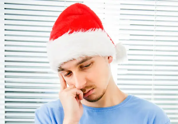Sad Young Man in Santa Hat on the Jalousie Background