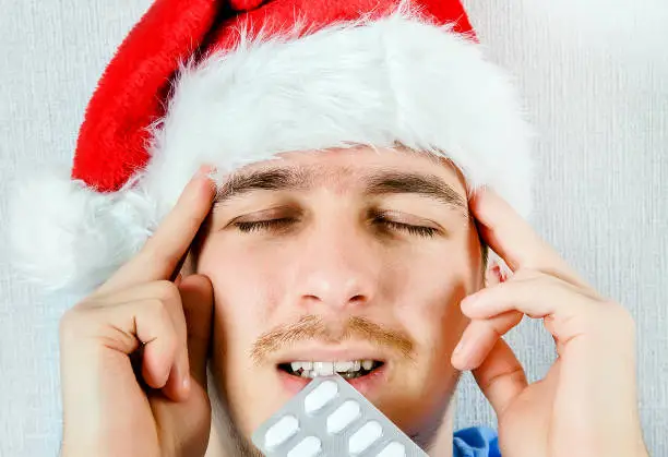 Sad Young Man in Santa Hat with a Pills in the Mouth closeup