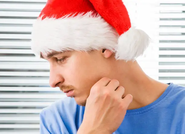 Sad Young Man in Santa Hat on the Jalousie Background closeup