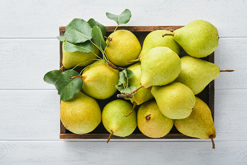 Pears. Fresh sweet organic pears with leaves in wooden box or basket on old white wooden retro table background. Autumn harvest of fruits. Top view. Food background.