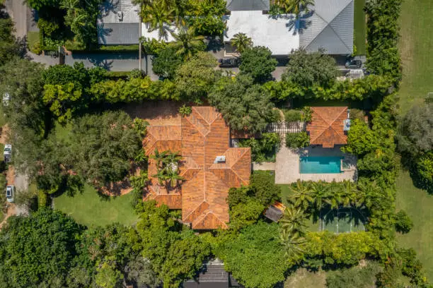 Colonial mansion with tropical landscape, blue sky, lots of bushes, driveway