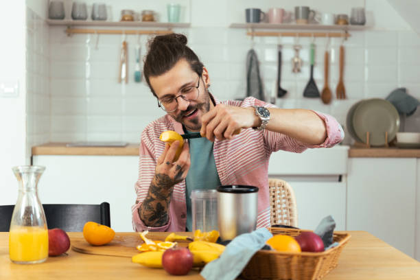 portrait of a young man chopping fruit and putting into a blender - blender apple banana color image imagens e fotografias de stock