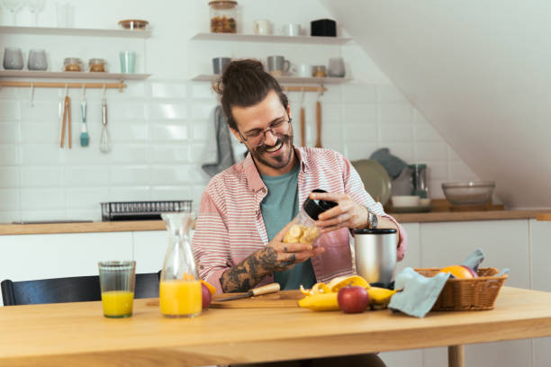 happy young man using a blender to make a smoothie - blender apple banana color image imagens e fotografias de stock