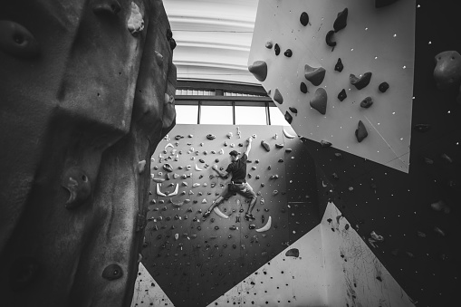 Athletic man climbing indoor wall.  Extreme sports and bouldering concept. Monochrome version.