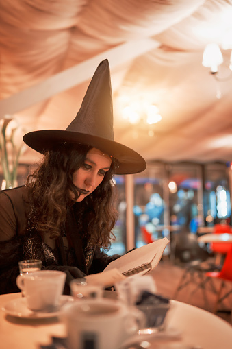 young latin woman dressed as a witch sitting and reading a notebook in a cafe