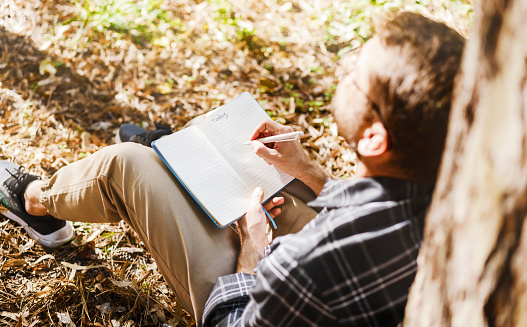 Adult man with eyeglasses sitting in the park and writing in his diary.